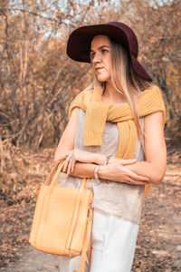 Young woman wearing hat standing against tree