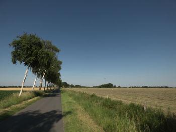 Road amidst field against clear sky