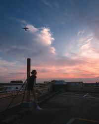 Teenage boy standing on terrace against sky during sunset