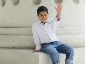 Portrait of boy sitting against while wall