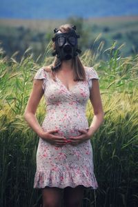 Portrait of pregnant of woman wearing gas mask while standing against plants