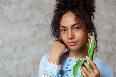 Portrait of smiling young woman holding tulip while standing against wall