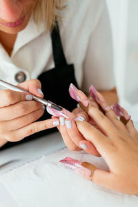 Crop unrecognizable female manicurist using brush while applying acrylic nail powder on tips of anonymous client in daylight in beauty salon