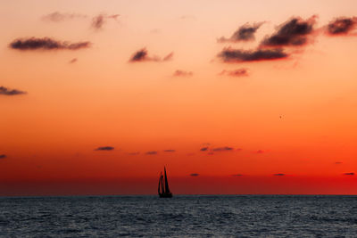Silhouette sailboat in sea against romantic sky at sunset