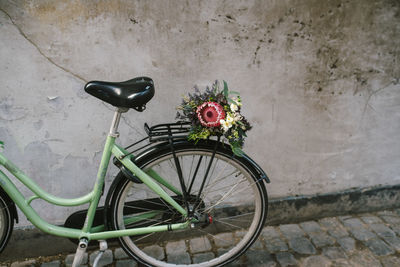Bicycle parked against wall with a bridal bouquet on the back seat