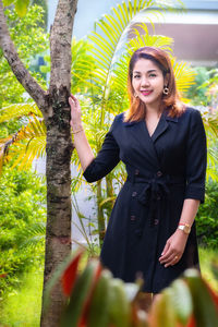 Smiling young woman standing against plants