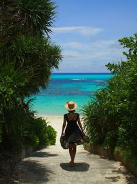 Rear view of woman walking towards sea against sky 