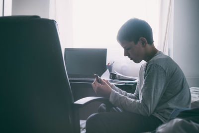 Side view of teenager using mobile phone and laptop