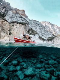 Man on rock by sea against mountain