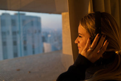 Woman listens to music with headphones by the window with a city view. mobile phone, technology, 