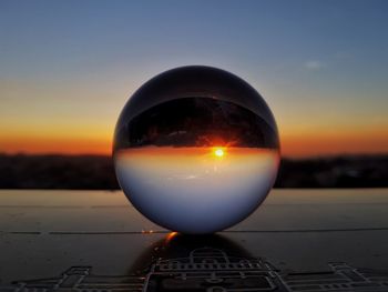 Close-up of crystal ball on landscape against sunset sky