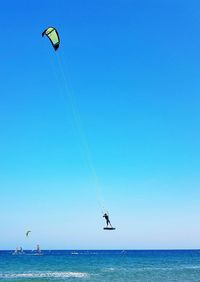 Low angle view of kite flying over sea against blue sky