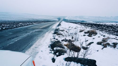 Snow covered road amidst field against sky