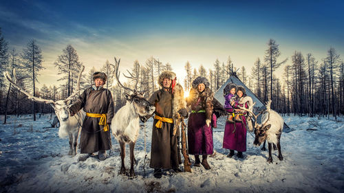 Portrait of family with reindeer on snow covered landscape during sunset