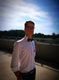 Young man wearing eyeglasses standing against sky