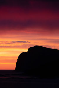 Silhouette rocks on sea against romantic sky at sunset