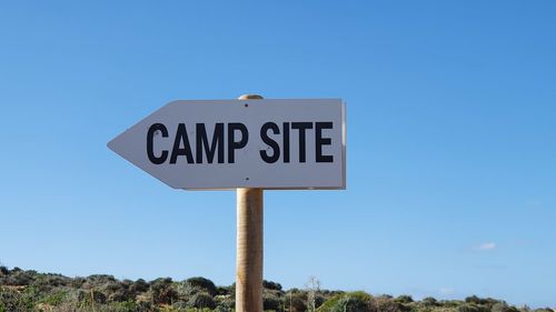 Low angle view of road sign against clear blue sky