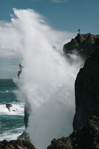 Waves splashing on rocks at shore against sky