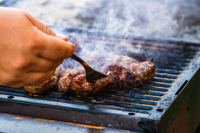 Cropped hand of person preparing meat on barbecue grill