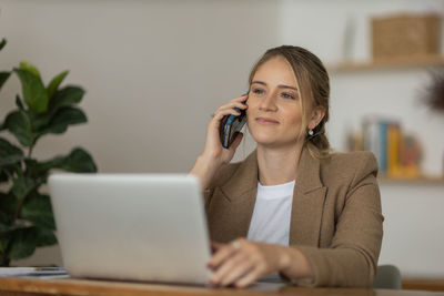 Woman working at home with laptop and speaking on mobile phone. home office. gray notebook 