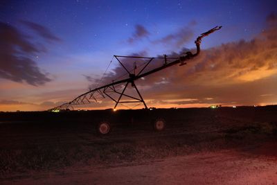 Silhouette electricity pylon on field against sky during sunset