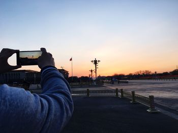 Cropped image of man photographing sunset in mobile phone