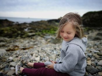 Cute girl sitting on rock at beach against sky