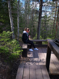 Girl using mobile phone while sitting on seat in forest