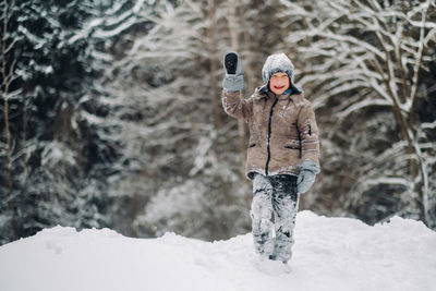 A cute boy stands in the forest in the snow in winter and laughs