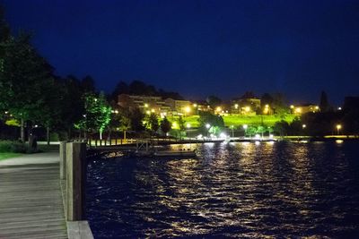 Illuminated city by river against sky at night