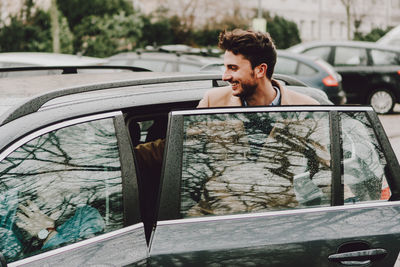 Happy young man entering wet car in city during rainy season
