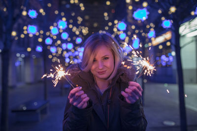 Portrait of woman holding illuminated sparkler at night