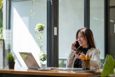 Businesswoman talking on mobile phone sitting with laptop at office