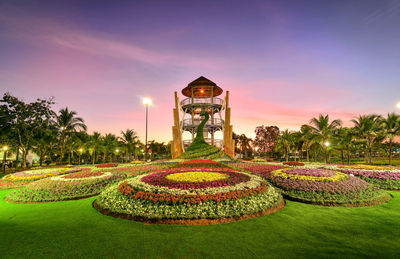 Panoramic view of illuminated garden by building against sky during sunset