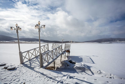 Snow covered railing by snowcapped mountain against sky