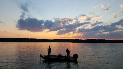 Silhouette people standing in lake against sky during sunset