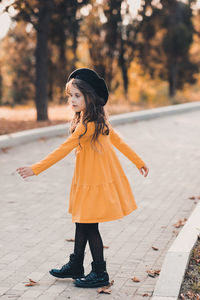 Stylish child girl 5-6 year old wear yellow dress and beret hat dancing in autumn park outdoor.