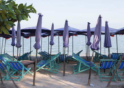 Empty chairs and tables on beach against sky