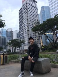 Full length of man sitting against modern buildings in city