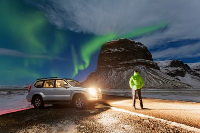 Rear view of man standing by car against sky