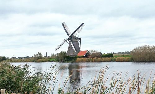 Traditional windmill by river against sky