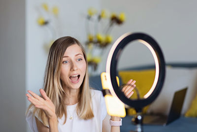 Young woman making photo or video content for social media with smartphone and light of ring lamp