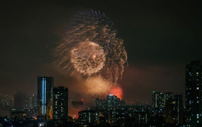 Firework display in city against sky at night