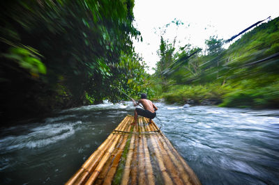 Rear view of man sailing wooden raft in river