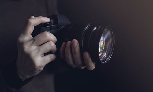 Midsection of man holding camera against black background