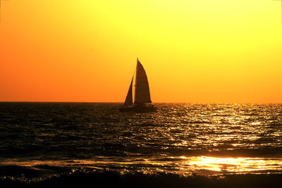 Silhouette sailboat in sea against orange sky