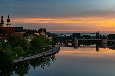 Scenic view of river by buildings against sky during sunset