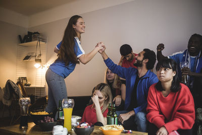 Cheerful blue team celebrating while loosing fans sitting upset at home