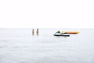 Distant view of female friends standing in sea against clear sky