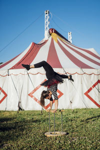 Female acrobat doing handstand on cane in front of circus tent